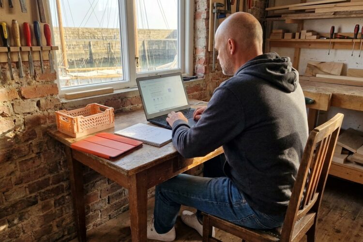 Handwerker Sönke sitzt an Schreibtisch in Werkstatt und optimiert sein Google Business Profile auf dem Laptop