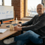 Solopreneur Office Schreibtisch mit Doppel-Monitor, Notizblock, Kaffeetasse und professioneller Tech-Peripherie auf Holz