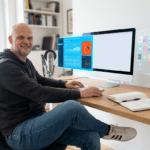 Funktionales Home-Office Marketing-Setup mit großem Monitor, Mikrofon, Notizbuch und schwebendem Dashboard mit Analyse-T